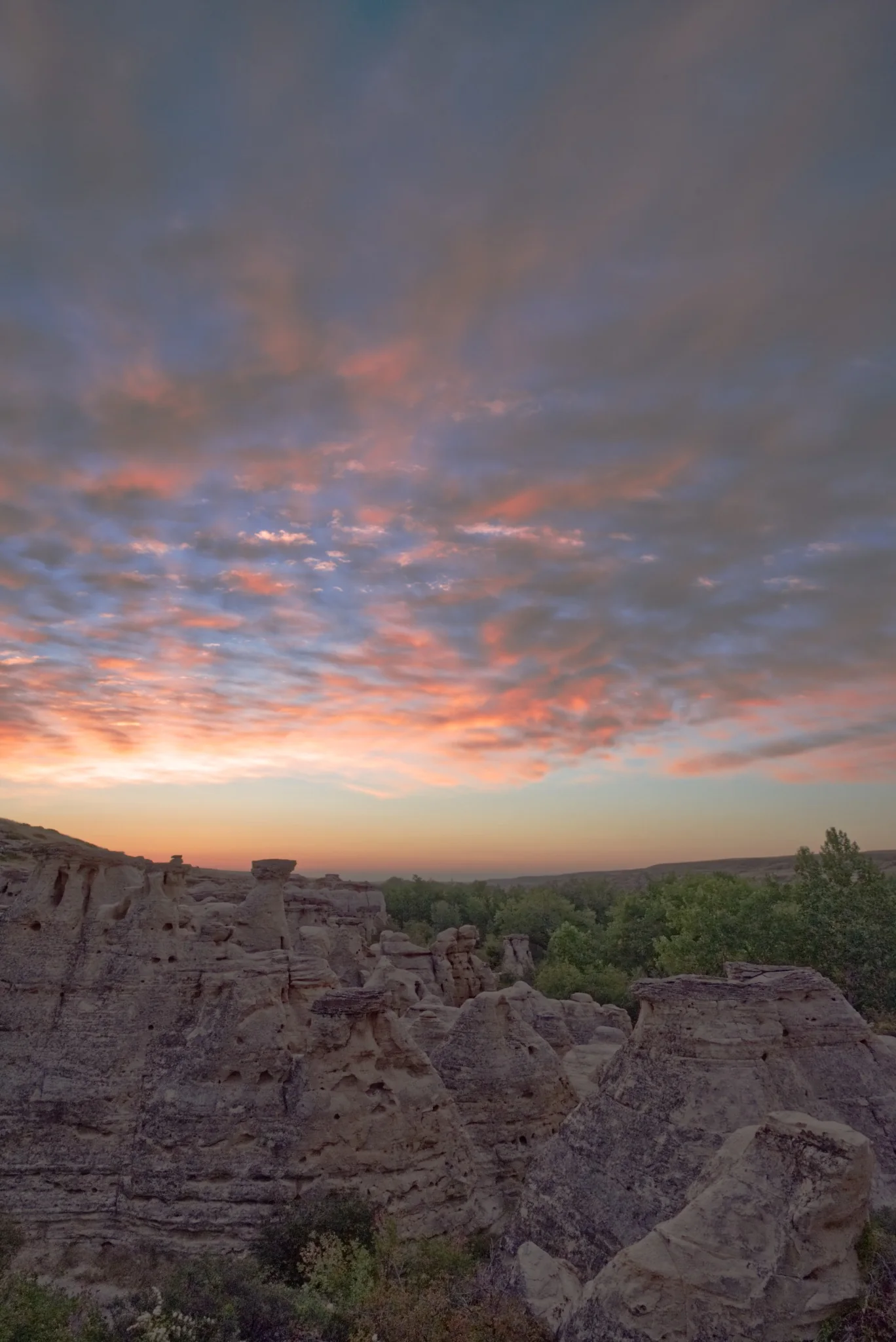Badlands hoodoos beneath a dramatic pink and orange sunset sky