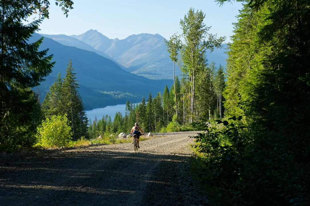 Bikepacker riding a remote mountain road above an Alberta lake