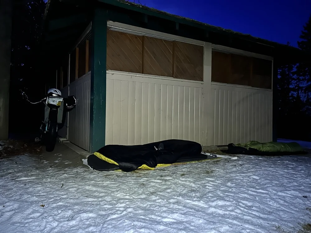 Sleeping gear laid out beside a small shelter on snowy ground at night