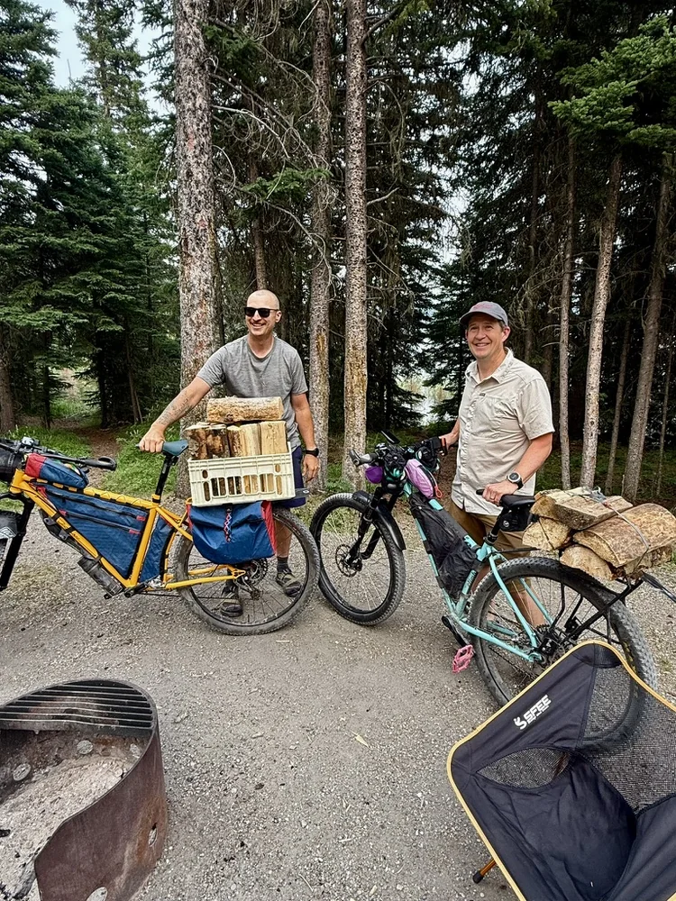 Two bikepackers with loaded bikes beside a forest campsite