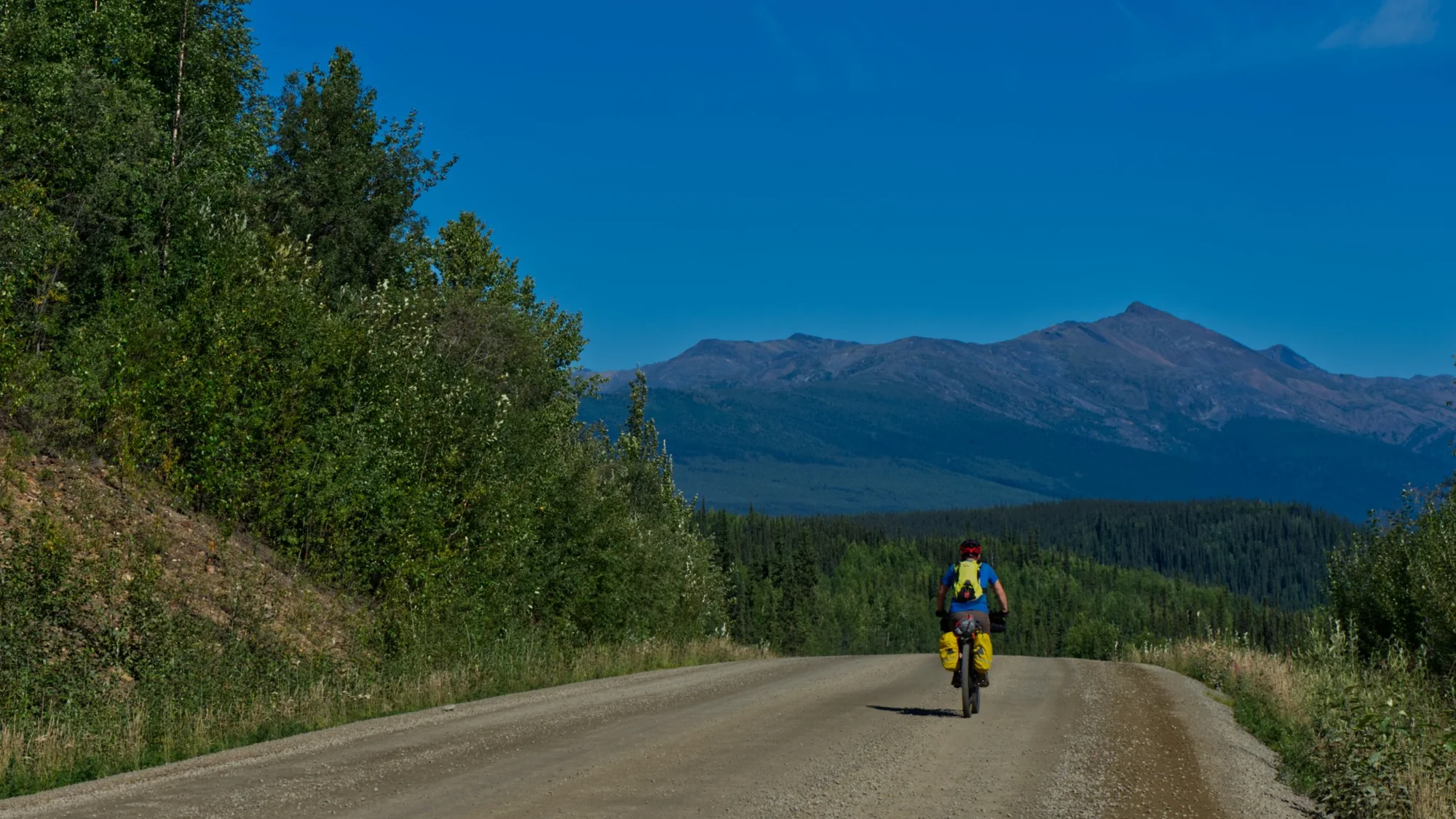 A bikepacker riding a remote gravel road toward the Alberta mountains