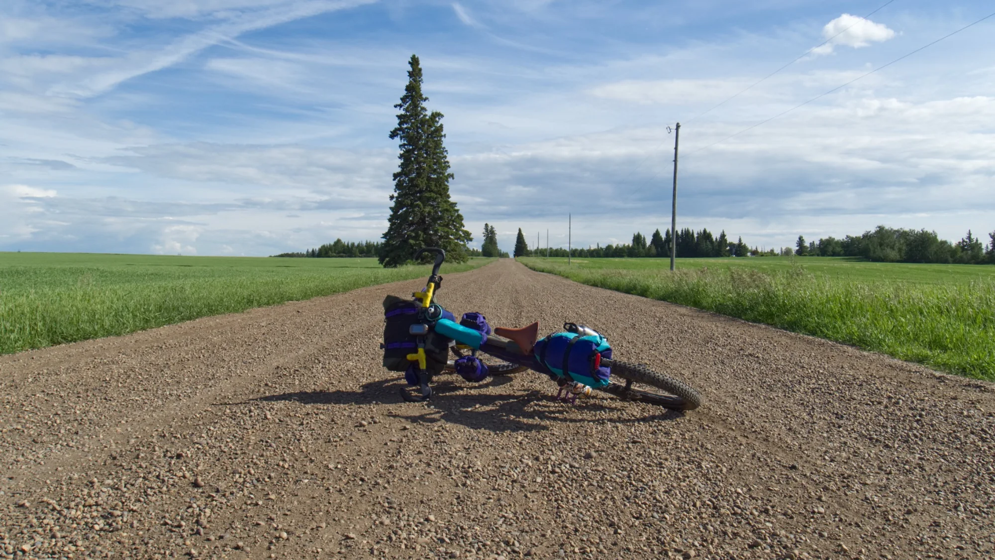A loaded bike resting on a long gravel road through open Alberta farmland