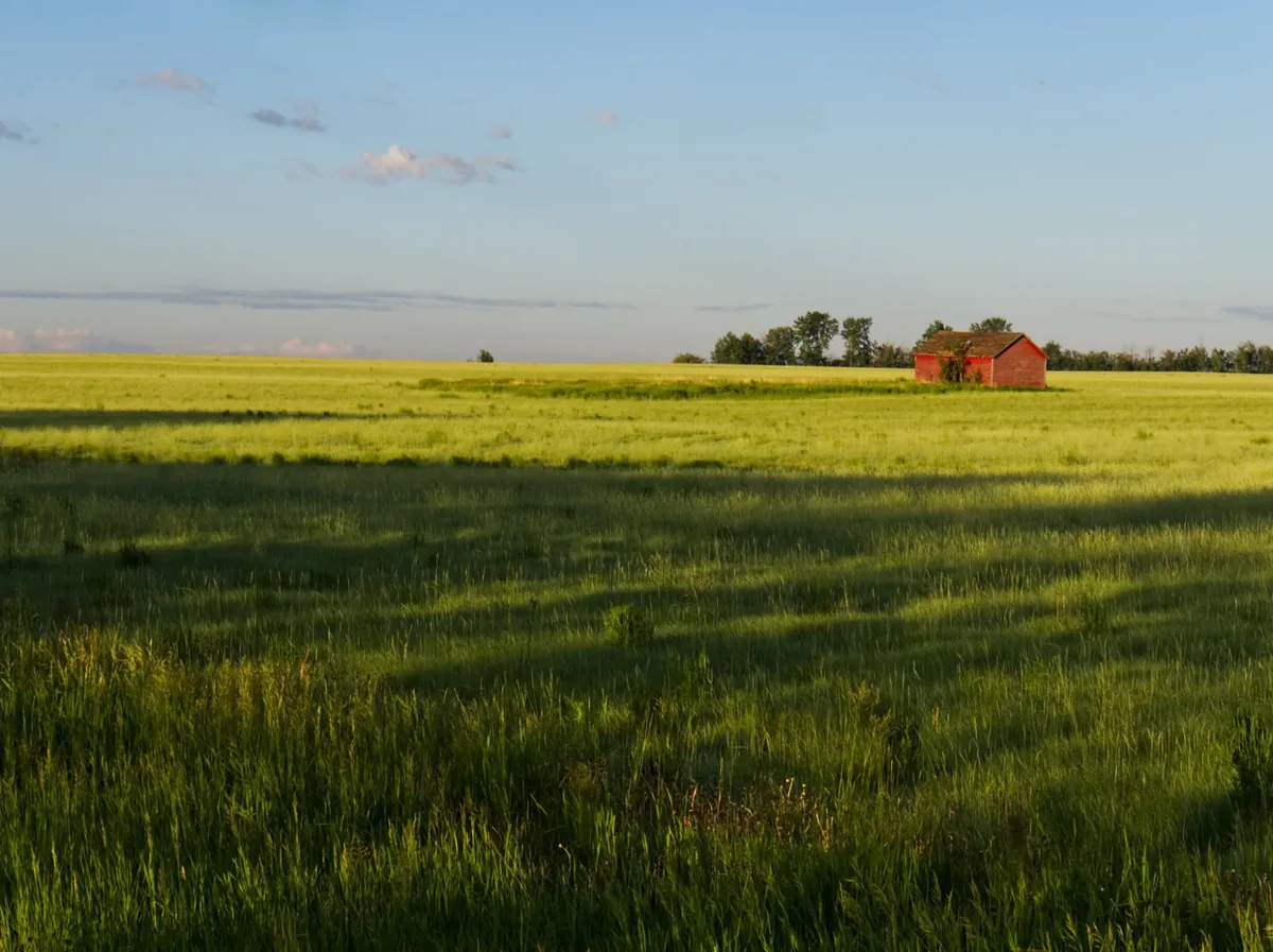 A red barn beside broad green prairie fields under an open sky